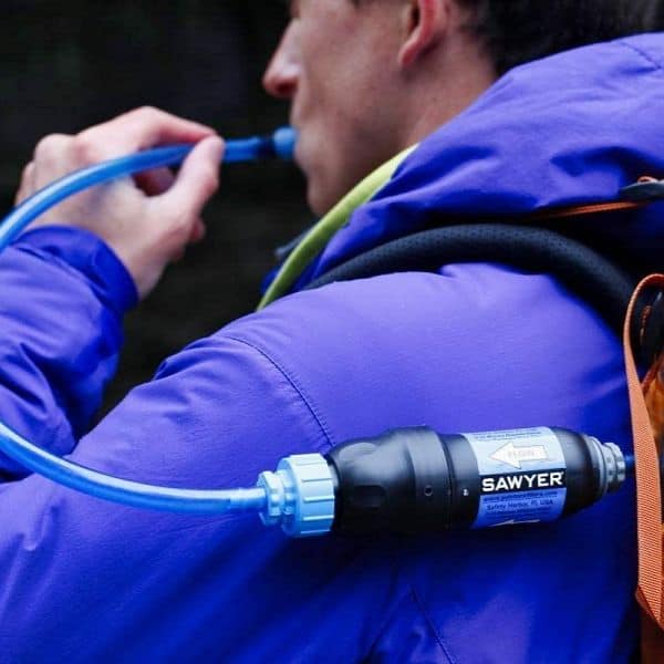 A backpacker sipping water from his Sawyer Squeeze fiter conveniently during camping