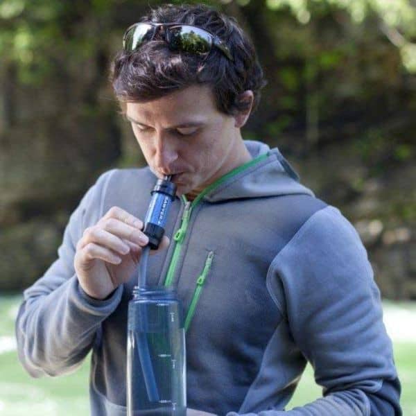 A man sipping water from his water bottle using the Sawyer Mini water filter
